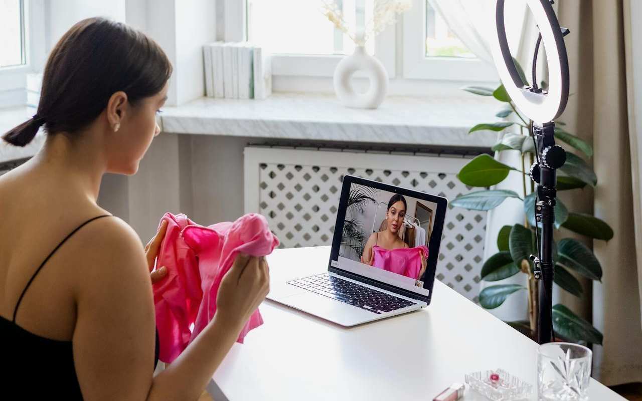 Devojka sedi ispred laptopa, snima se i pokazuje odeću