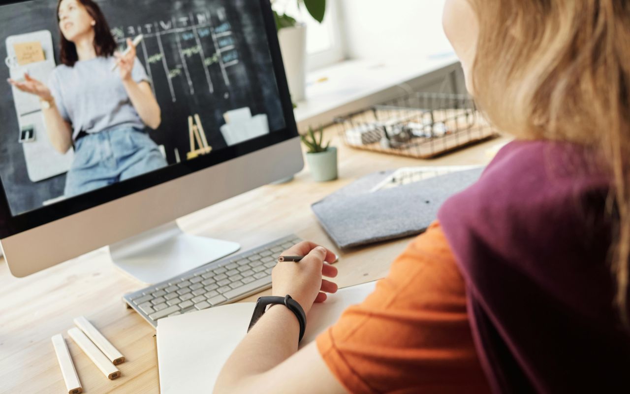 Devojka gleda edukativni sadržaj na monitoru i zapisuje beleške