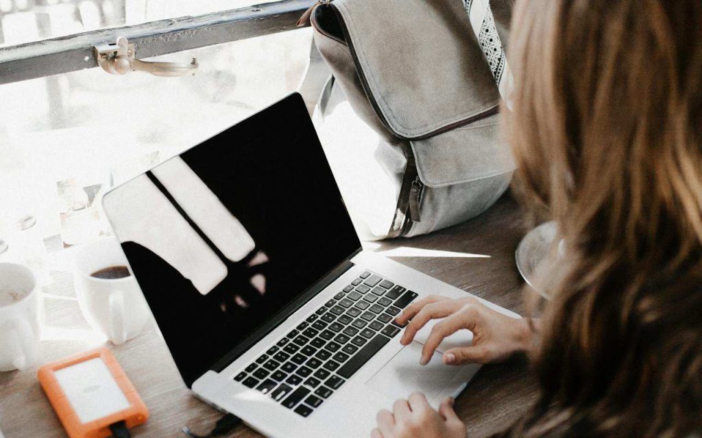 Devojka sedi za stolom i kuca na laptopu.