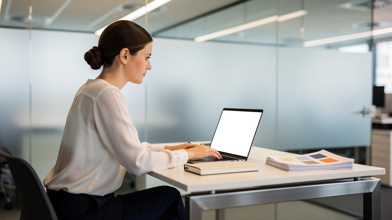 Žena sedi za stolom u kancelariji i radi na laptopu
